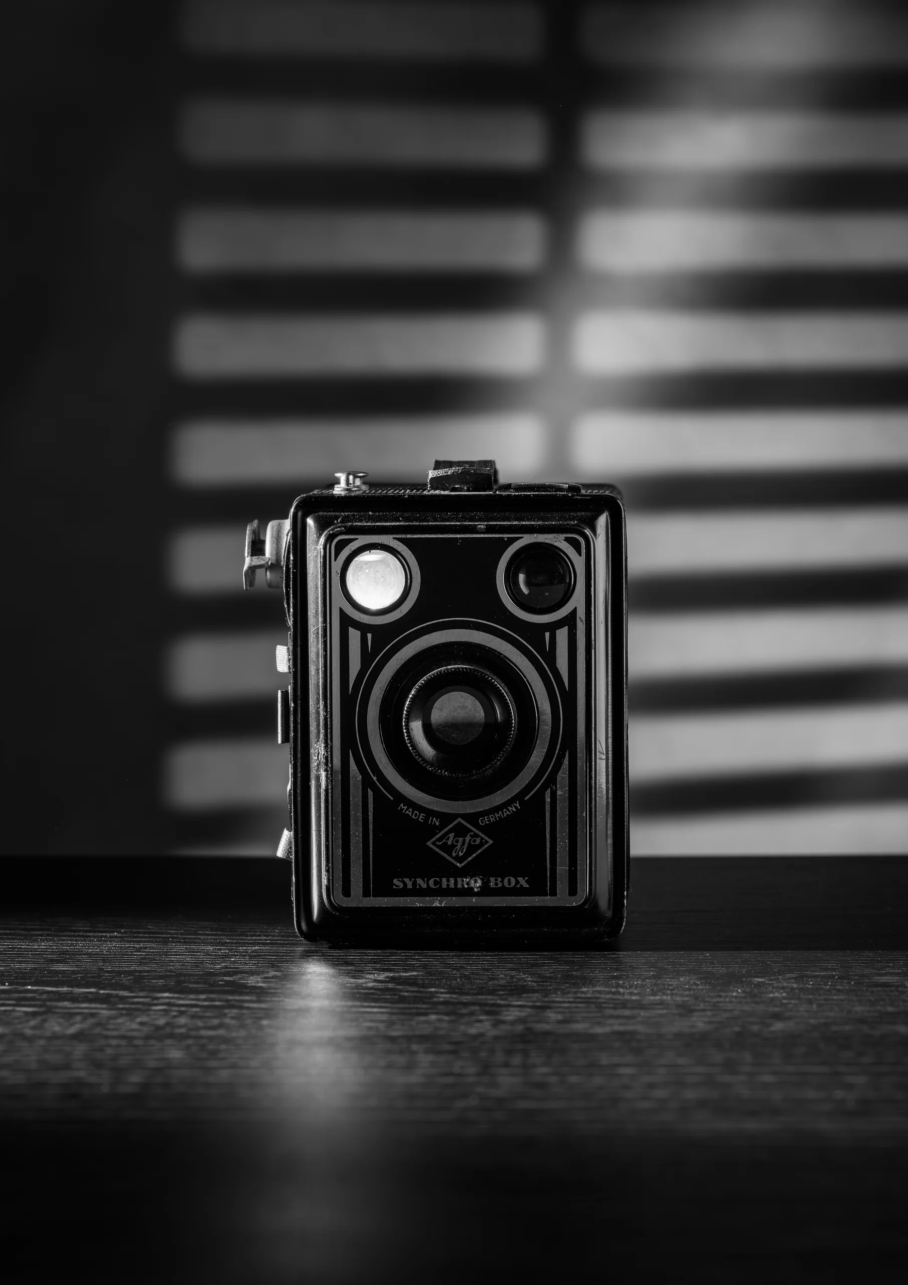 Zwart-wit stilleven van een boxcamera met lichtstrepen van jaloezieën
