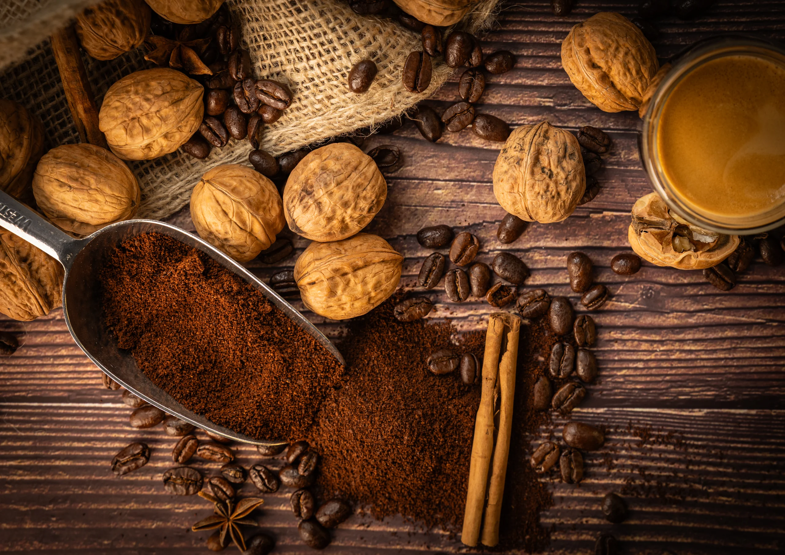Stilleven van gemalen koffie in een schep met walnoten, kaneel en koffiebonen op hout