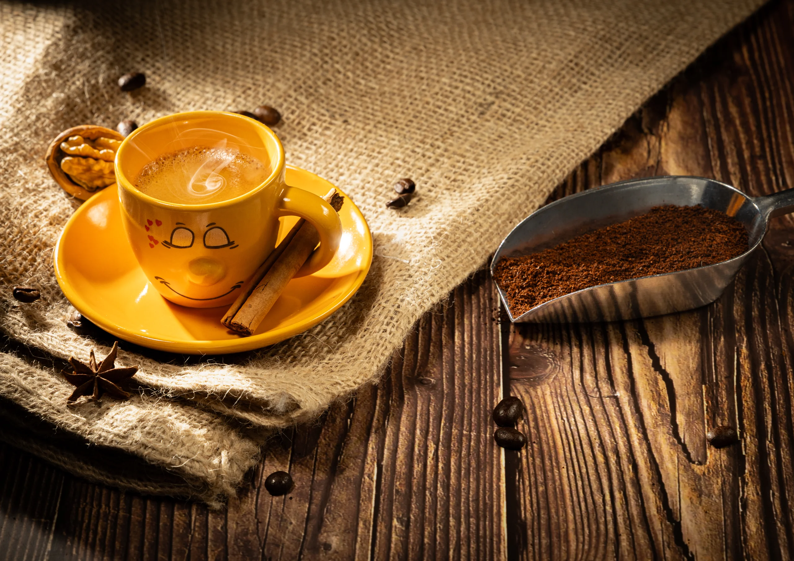 Stilleven van een geel kopje koffie op jute naast een schep gemalen koffie